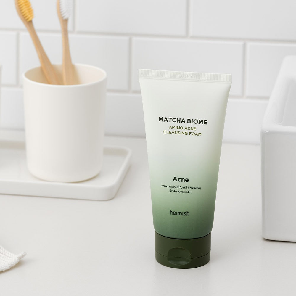 HEIMISH Matcha Biome Amino Acne Cleansing Foam 150g on bathroom counter with toothbrushes, featuring soothing matcha skincare.