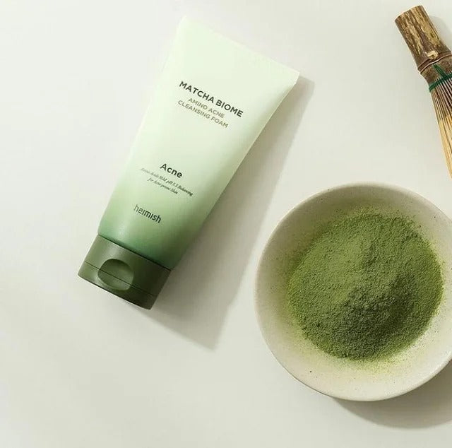 HEIMISH Matcha Biome Amino Acne Cleansing Foam 150g next to a bowl of matcha powder and wooden whisk