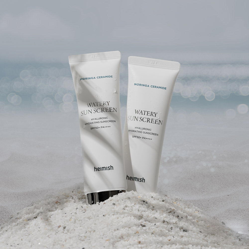 HEIMISH Moringa Ceramide Hyaluronic Hydrating Watery Sunscreen 50ml tubes on sandy beach with ocean backdrop