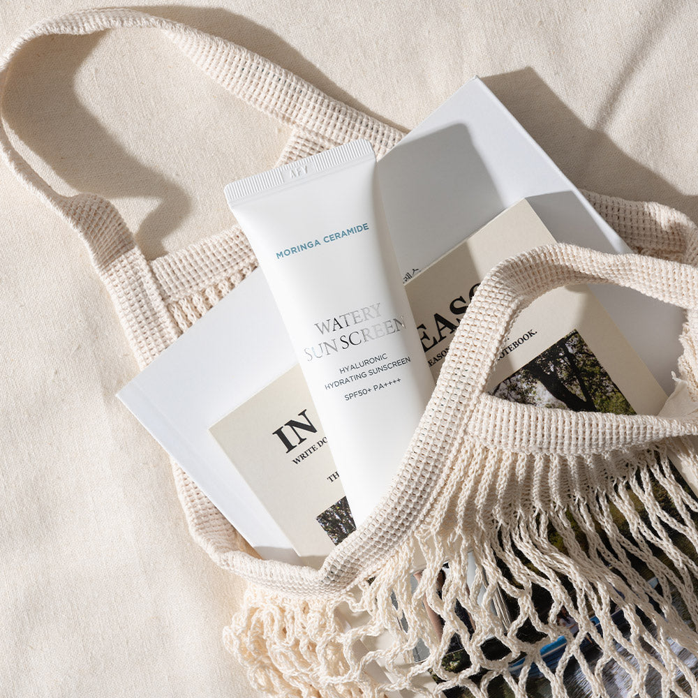HEIMISH Moringa Ceramide Hyaluronic Hydrating Watery Sunscreen 50ml in a stylish woven bag with natural sunlight