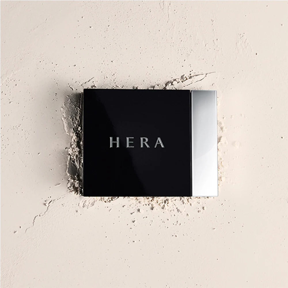 HERA Airy Powder Primer 8.5g compact case on a textured powder surface