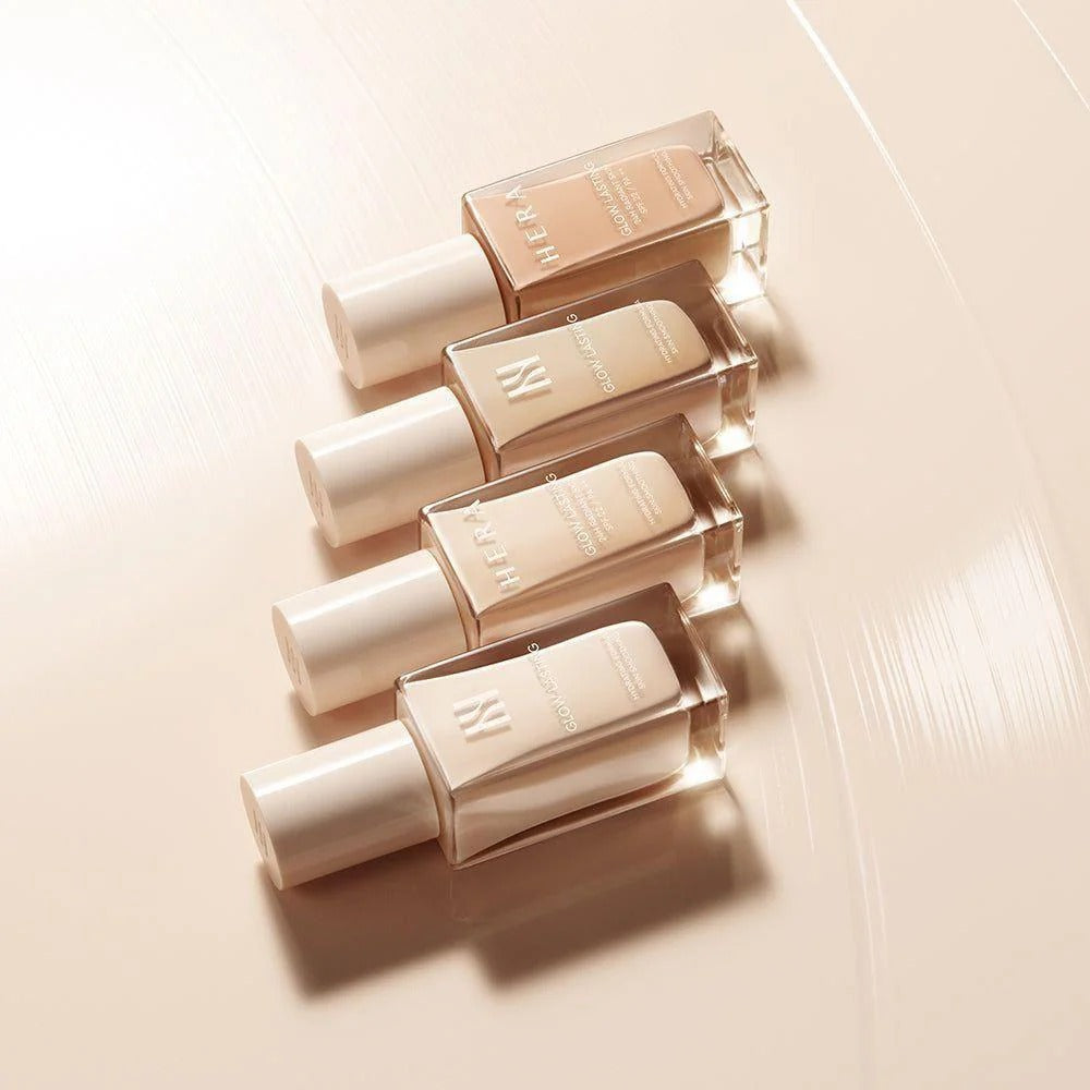 HERA Glow Lasting 24H Radiant Skin SPF22 PA++ 30g foundation bottles on a glossy surface