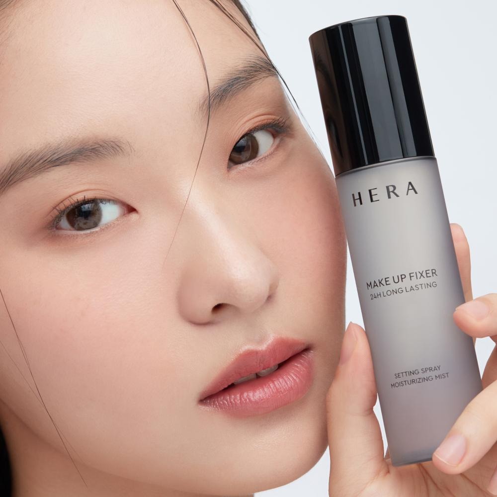 Close-up of woman holding HERA Make Up Fixer 80ml, luxurious setting spray for long-lasting makeup finish.