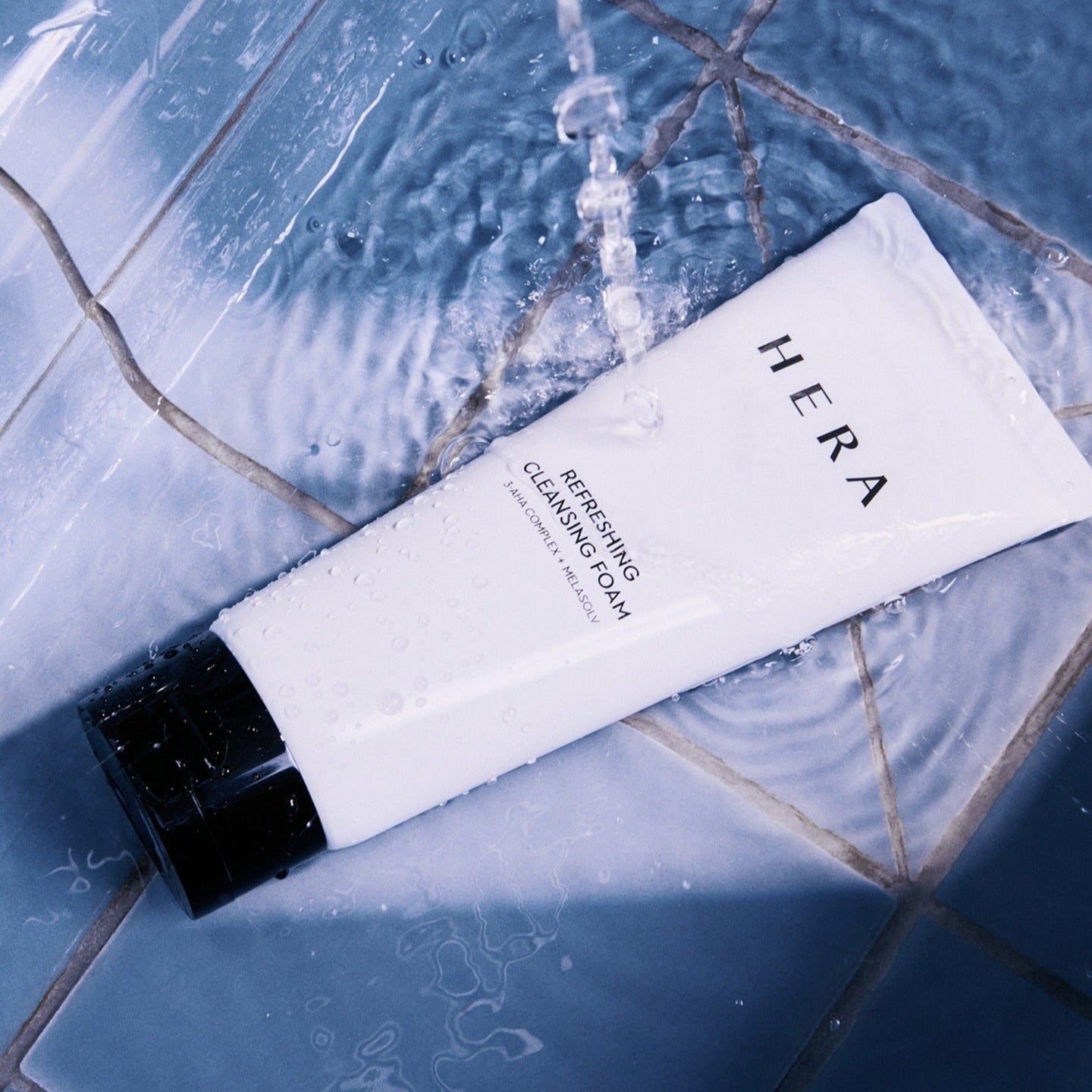 HERA Refreshing Cleansing Foam 160g on wet tiles under running water highlighting the skincare product's fresh appeal.