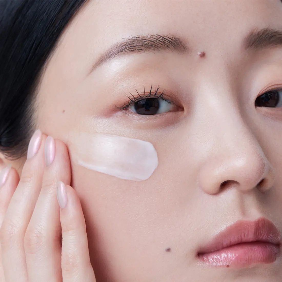 Woman applying HERA Rejuvanate Ampoule Cream 50ml on her cheek, showcasing smooth skin and hydration effect.