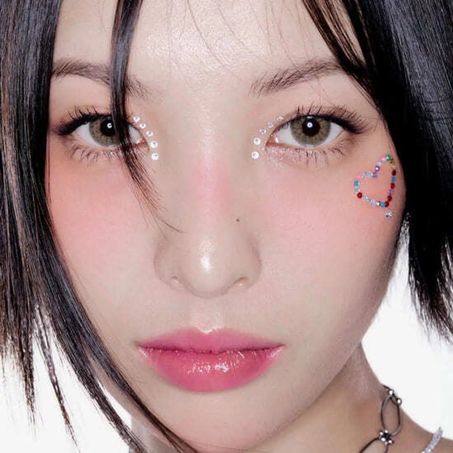 Close-up of a person with sparkling eye makeup and a colorful heart on the cheek.