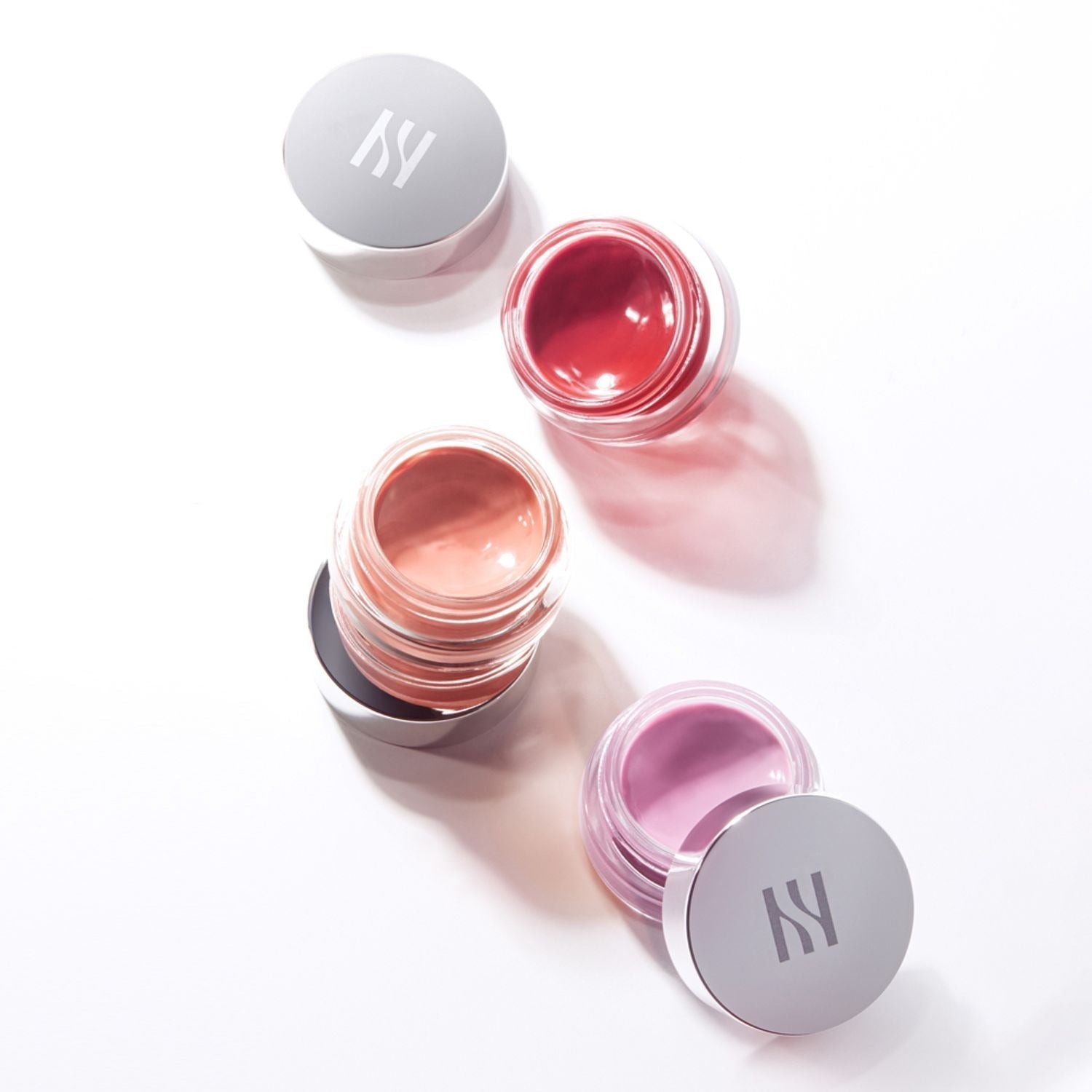 Open jars of HERA Sensual Lip & Cheek 7g in various shades on a white background.