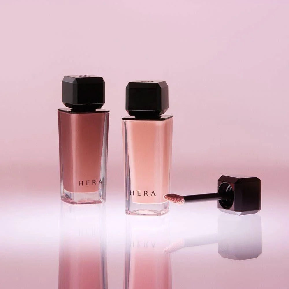 HERA Sensual Nude Gloss 5g with two elegant bottles and applicator on a pink background