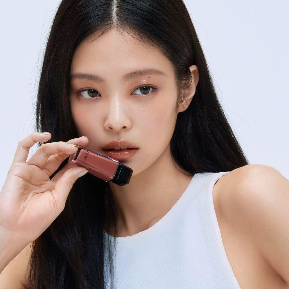 Woman holding HERA Sensual Nude Gloss 5g, showcasing the lip gloss color and design.