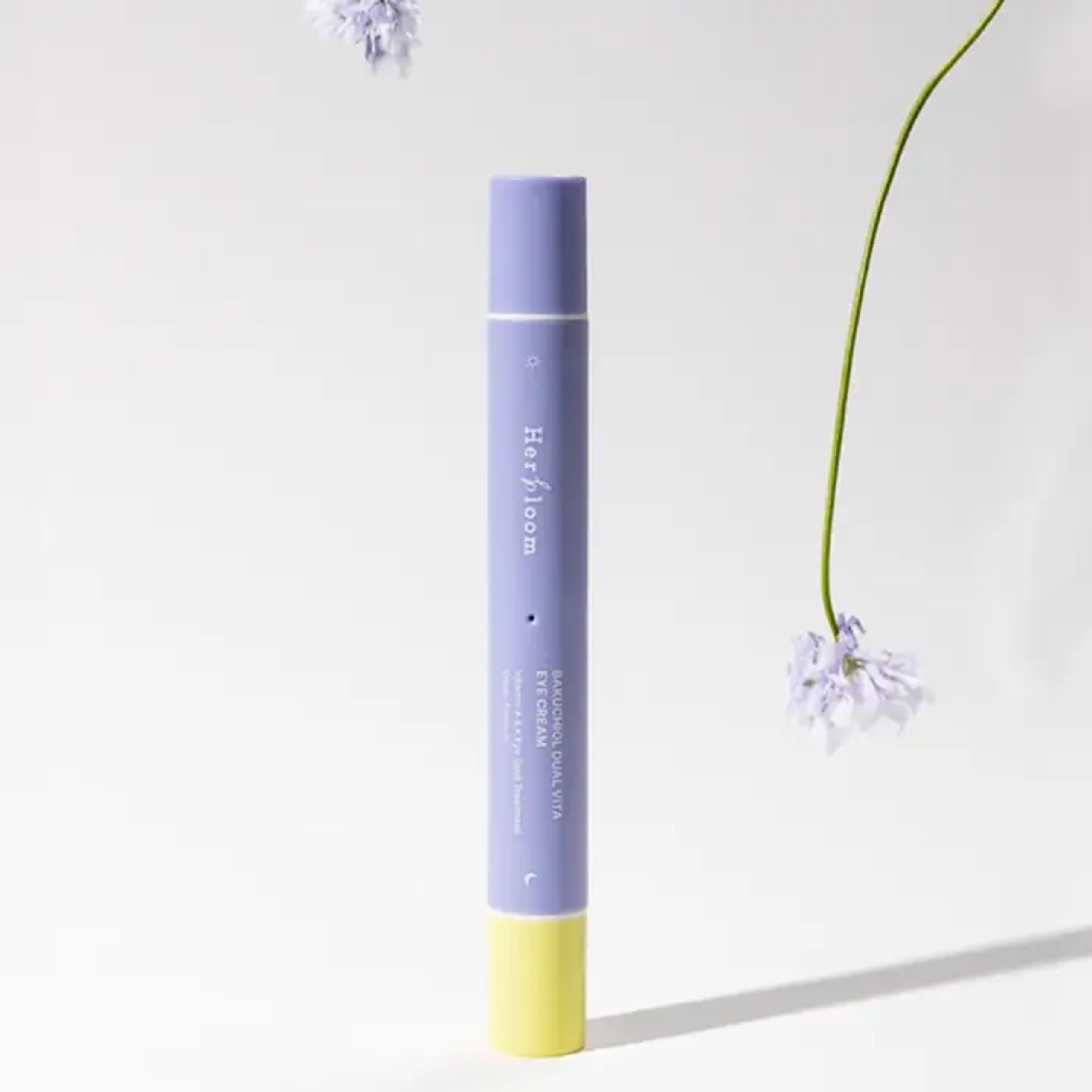 HERBLOOM Bakuchiol Dual Vita Eye Cream in a sleek purple and yellow tube surrounded by delicate flowers.
