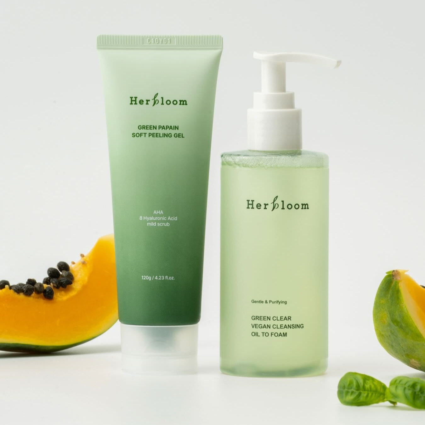 HERBLOOM Green Papain Soft Peeling Gel 120g and Green Clear Vegan Cleansing Oil to Foam with papaya slices displayed elegantly.