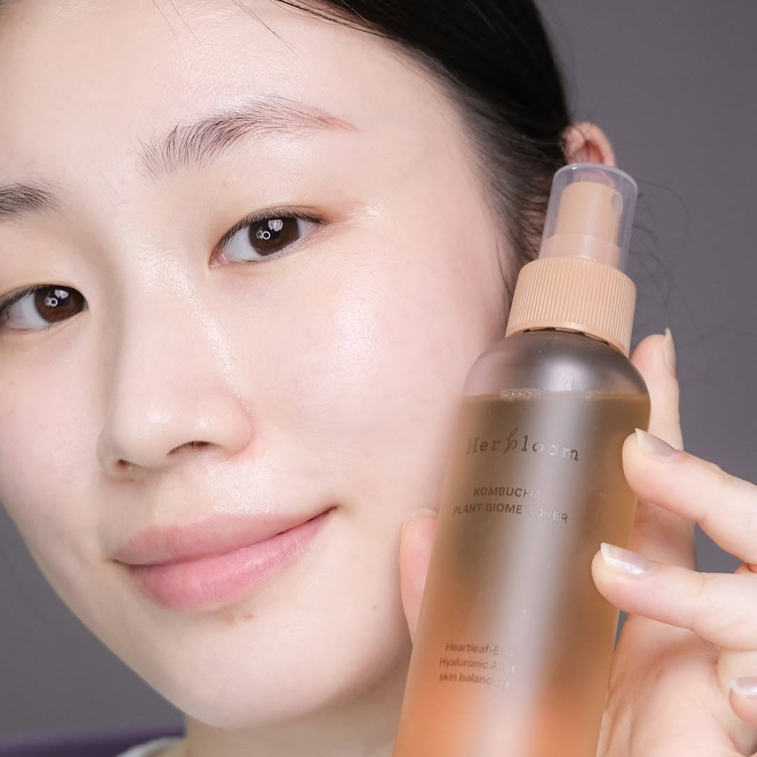 Smiling person holding HERBLOOM Kombucha Plant Biome Toner 150g bottle, showcasing skincare product with a natural glow.