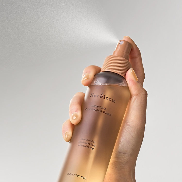 Hand holding HERBLOOM Kombucha Plant Biome Toner 150g spray bottle for skin health