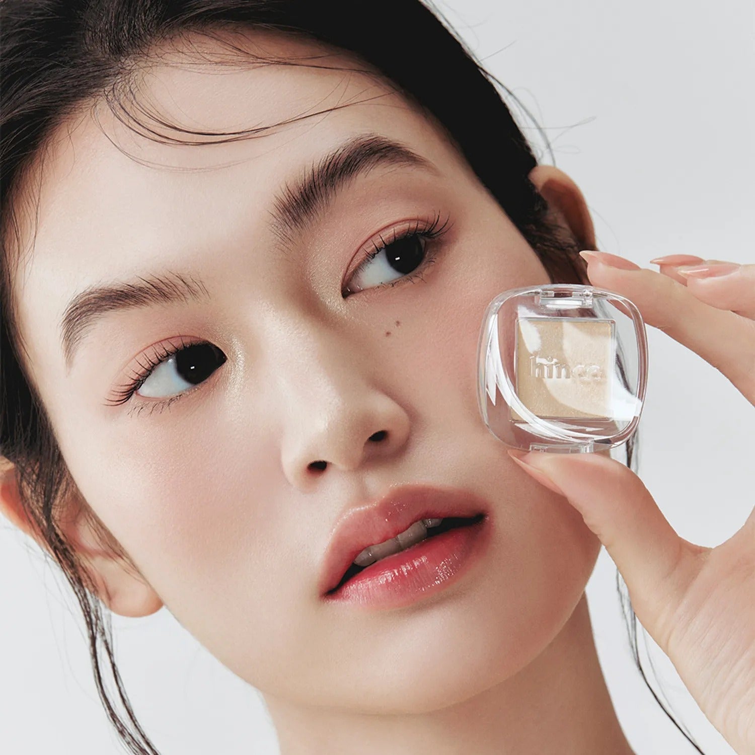 Close-up of a woman holding HINCE Single Eyeshadow, emphasizing a neutral makeup look with the product.