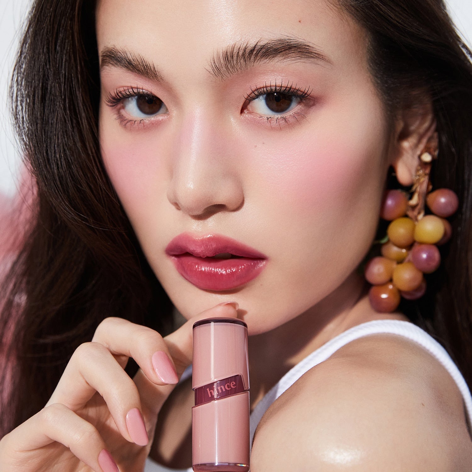 Model showcasing HINCE Ro Glow Gel Tint with rosy lips and cheek color, holding the product elegantly, highlighting its vibrant hue.