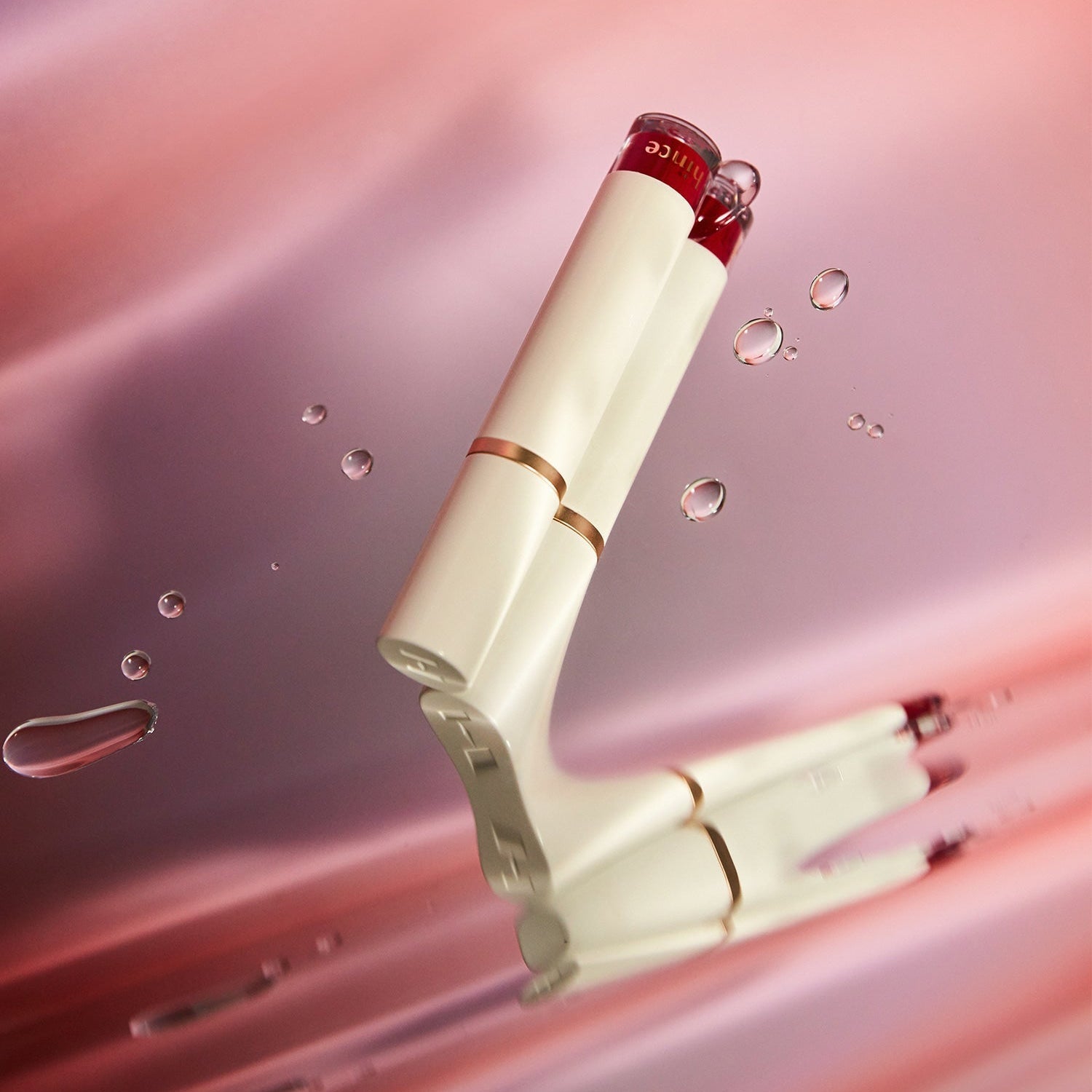 HINCE Mood Enhancer Water Liquid Glow product displaying elegant design with water droplets reflecting radiant glow on a pink background.