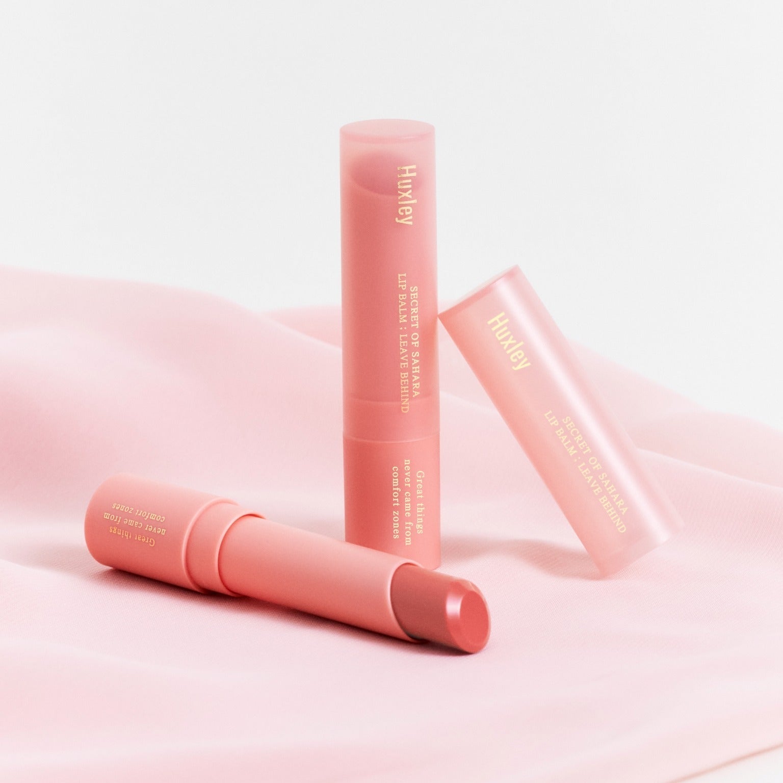 HUXLEY Lip Balm Leave Behide in elegant pink packaging on soft fabric, showcasing premium lip care and hydration.