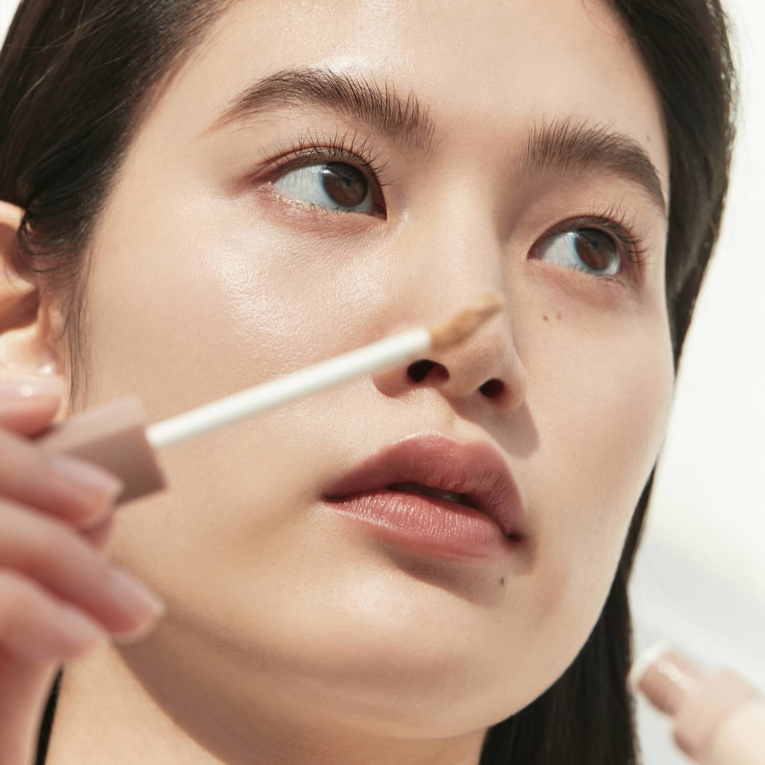 Woman applying HINCE Second Skin Cover Concealer for flawless complexion close-up.