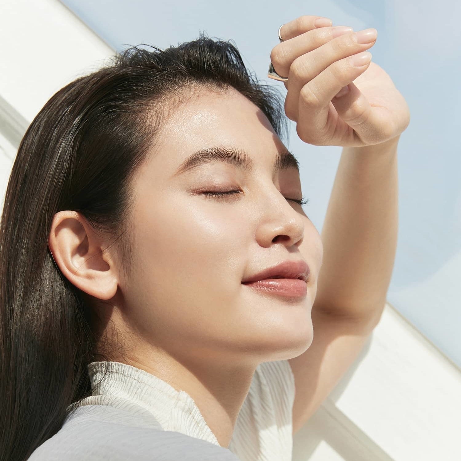 Woman enjoying sunlight outdoors with radiant skin, showcasing effects of HINCE Second Skin Cover Concealer, eyes closed in relaxation.